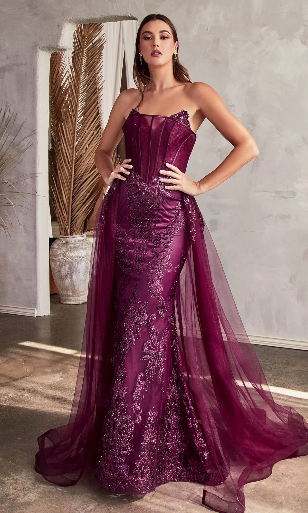 A woman poses indoors with hands on hips, wearing the Glitter-Print Strapless Long Prom Dress J858 in merlot, featuring lace detailing, sheer panels, and tulle overlay accents against a neutral background.